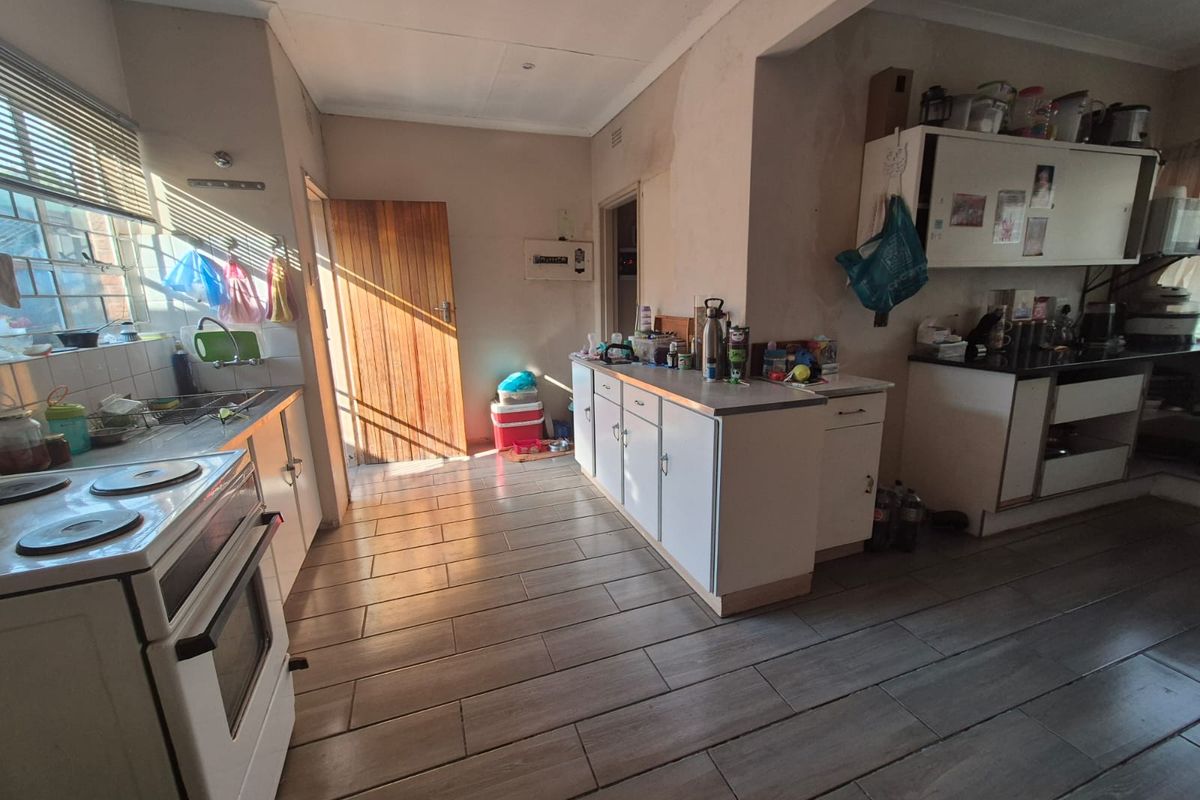 A functional kitchen featuring built-in cabinetry, an electric stove, and tiled flooring, currently requiring cosmetic updates and wall repairs.