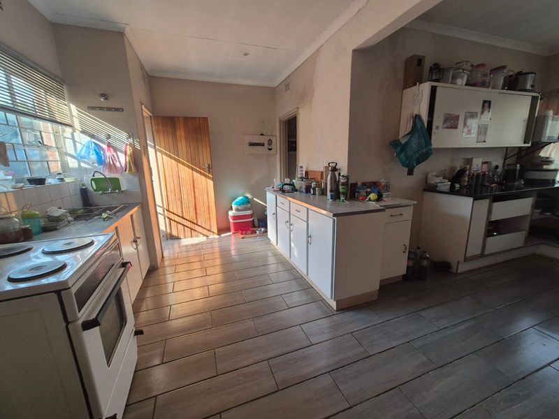 A functional kitchen featuring built-in cabinetry, an electric stove, and tiled flooring, currently requiring cosmetic updates and wall repairs.