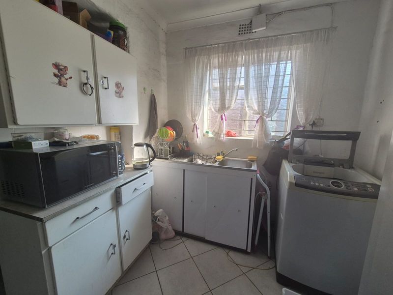 A compact laundry area featuring built-in cabinetry, a stainless steel sink, and tiled flooring, currently showing signs of wear and requiring cosmetic updates.