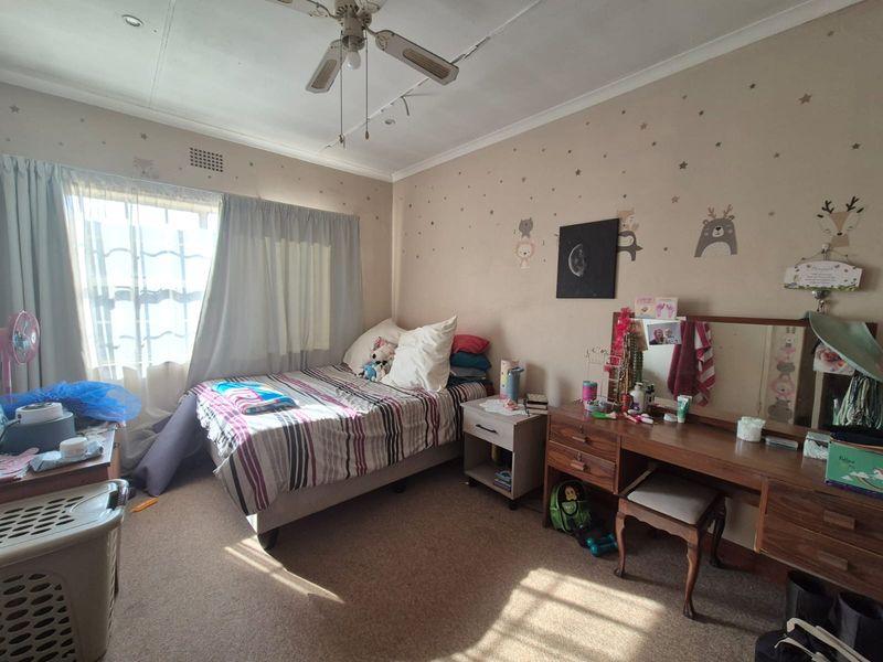 A bedroom featuring carpeted flooring and a ceiling fan, showing signs of wear including a visible crack in the ceiling.