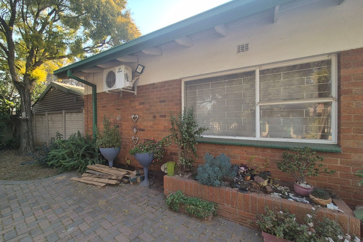 Rear exterior view of the house featuring a brick facade, paved patio area, built-in brick planter box, and wall-mounted air conditioning unit.