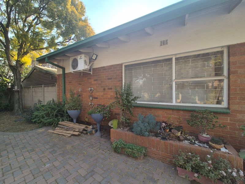Rear exterior view of the house featuring a brick facade, paved patio area, built-in brick planter box, and wall-mounted air conditioning unit.