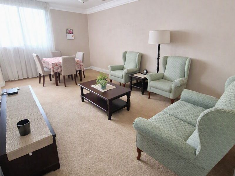 A comfortable living room area featuring neutral wall tones, crown molding, and carpeted flooring, providing a functional space for relaxation.