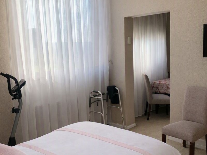 A bedroom featuring neutral wall finishes, fitted curtains, and a wall-mounted television, with an adjacent space visible through the doorway.