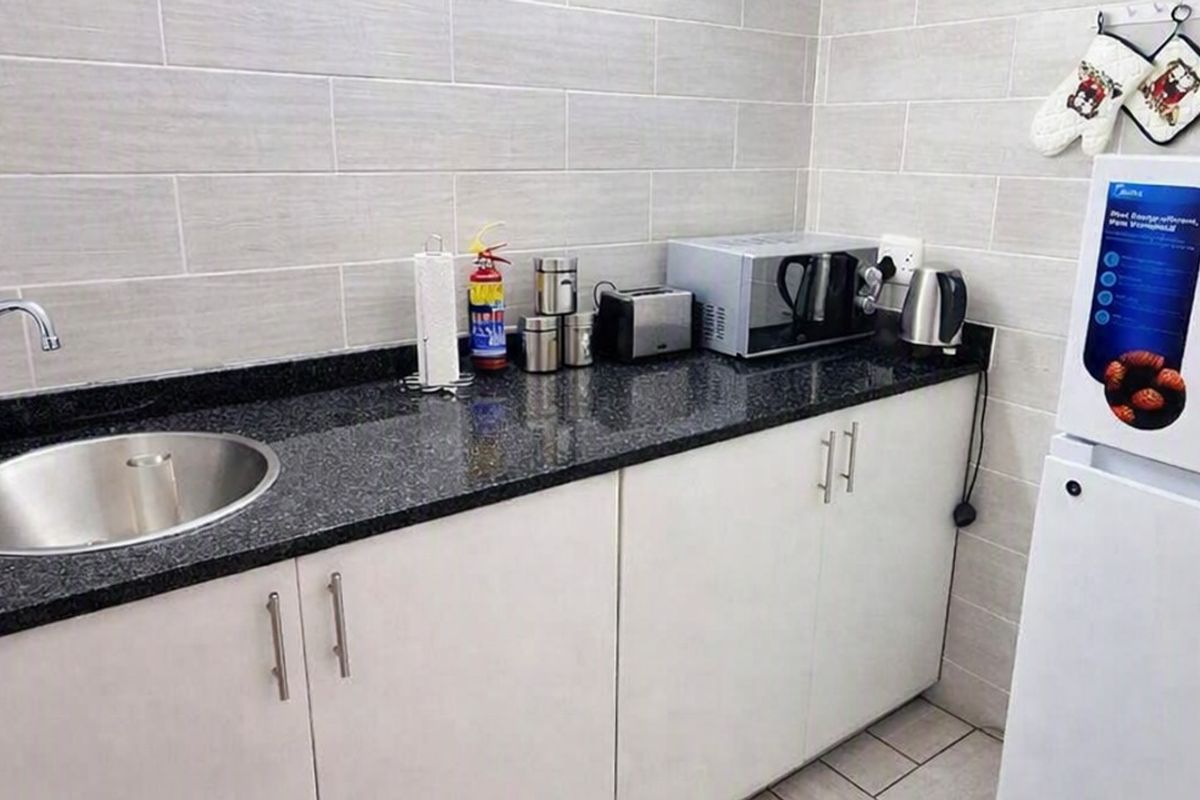 Compact kitchen area featuring white cabinetry, dark granite countertops, a stainless steel sink, and modern tiled splashbacks.
