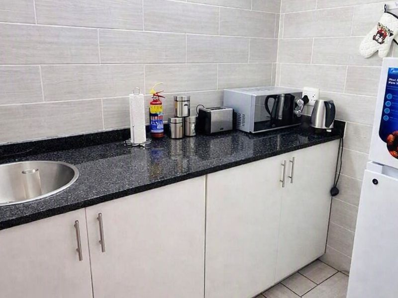 Compact kitchen area featuring white cabinetry, dark granite countertops, a stainless steel sink, and modern tiled splashbacks.