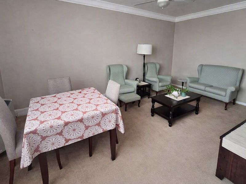 A living room area featuring neutral wall tones, carpet flooring, and a ceiling fan, providing a functional and comfortable space.