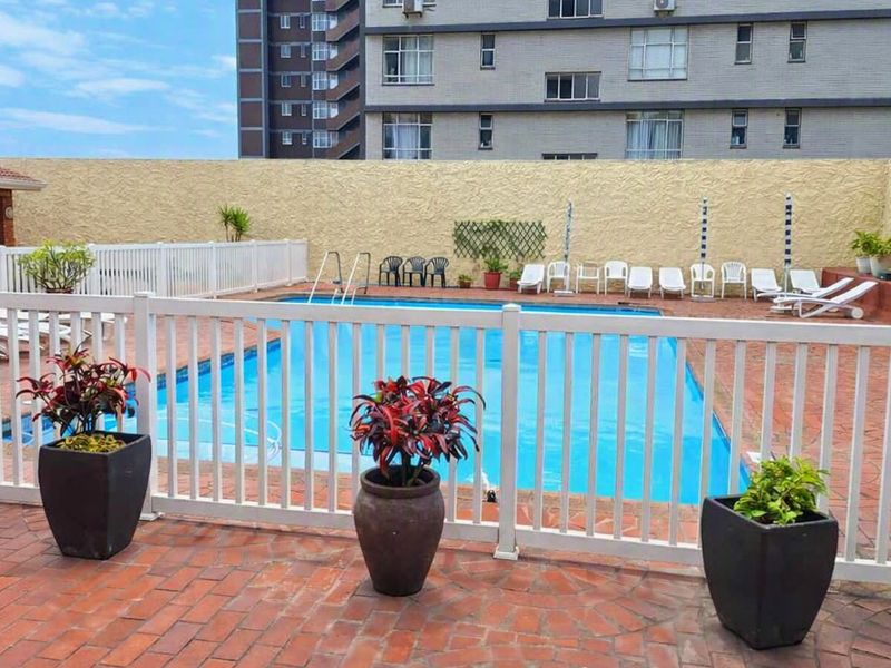 A communal swimming pool area featuring brick paving, safety fencing, and a surrounding retaining wall within a retirement village setting.