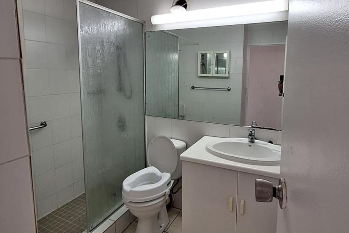 A functional bathroom featuring a shower enclosure, vanity cabinet with basin, and wall-mounted mirror, suitable for modernization.