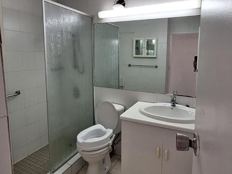 A functional bathroom featuring a shower enclosure, vanity cabinet with basin, and wall-mounted mirror, suitable for modernization.