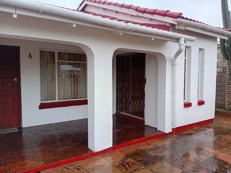 Front entrance of the house featuring a covered patio, security gate, and stone paved flooring under a tiled roof.