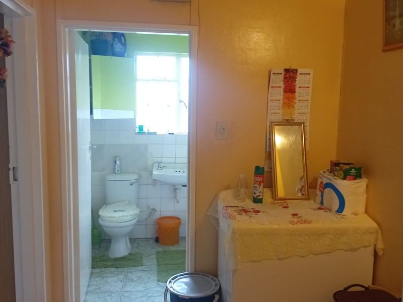 A functional bathroom featuring a standard toilet and wall-mounted basin, accessible from an adjacent hallway with tiled flooring and decorative ceiling cornicing.