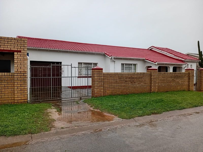 Front elevation of a single-story house featuring a red tiled roof, brick boundary wall, and a metal driveway gate.