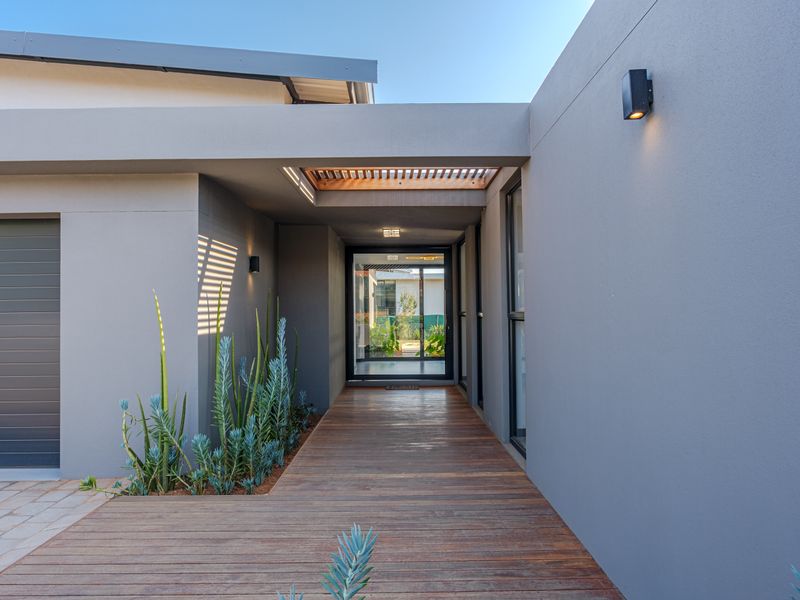 Modern entrance featuring timber decking, a covered walkway with a timber pergola, and sleek grey exterior finishes.
