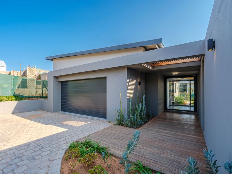 Modern front facade featuring a sleek garage door, timber decking entrance, and paved driveway with contemporary architectural lines.