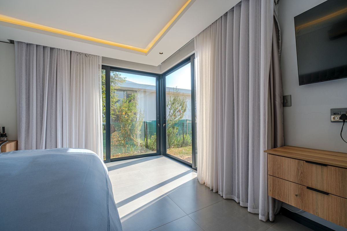 Modern bedroom featuring large corner sliding glass doors, recessed ceiling lighting, and sleek tiled flooring with built-in cabinetry.