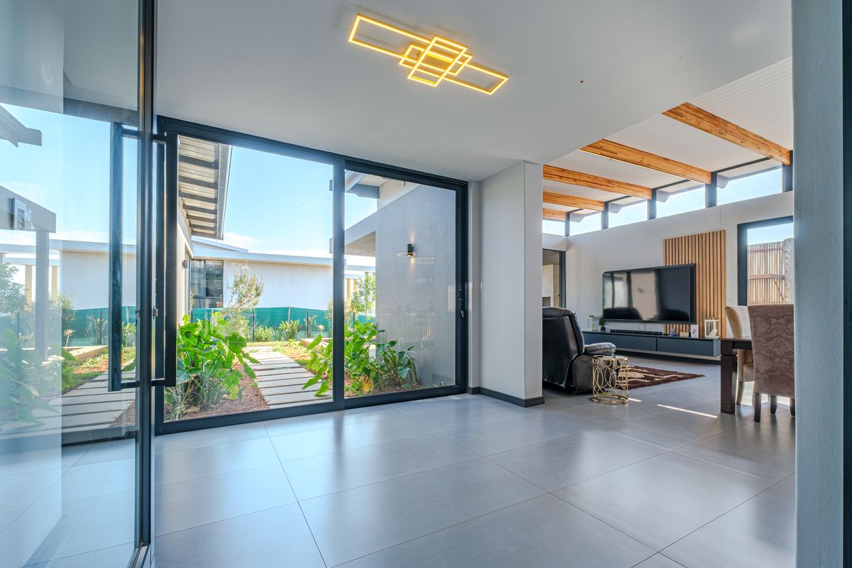 Modern open-plan living area featuring large format floor tiles, exposed timber beams, clerestory windows, and seamless access to the garden through sliding glass doors.