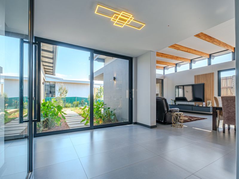 Modern open-plan living area featuring large format floor tiles, exposed timber beams, clerestory windows, and seamless access to the garden through sliding glass doors.