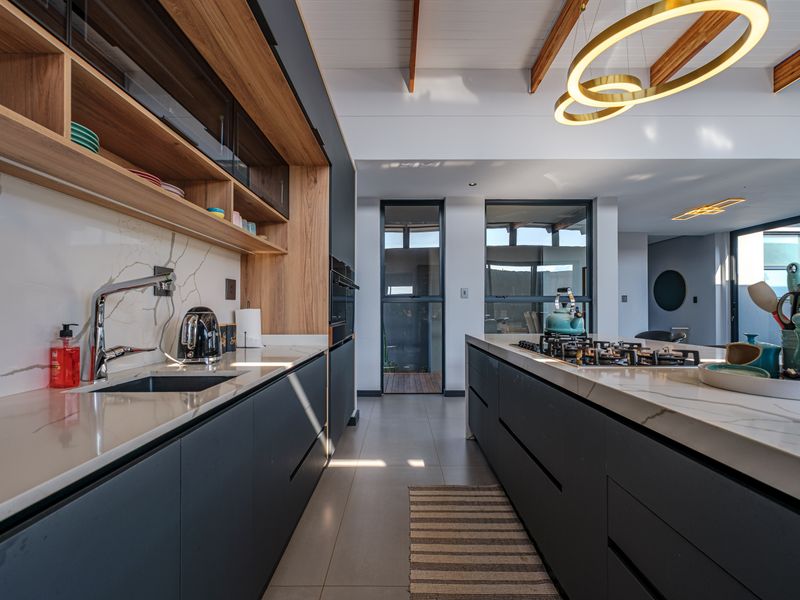 Modern kitchen featuring dark cabinetry, stone benchtops, gas cooktop, and exposed timber ceiling beams, creating a sophisticated and functional culinary space.