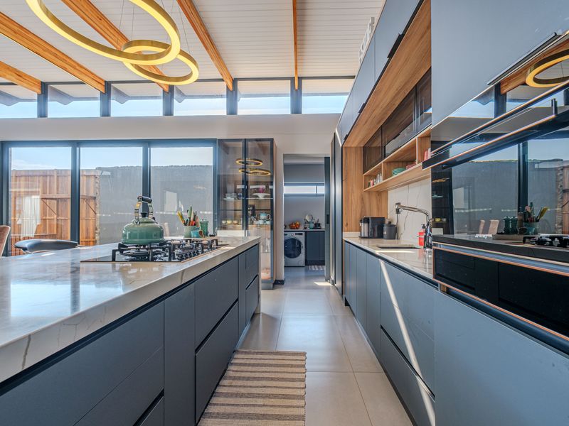 Modern kitchen featuring a large island with gas hob, stone countertops, integrated cabinetry, and high ceilings with exposed timber beams and clerestory windows.