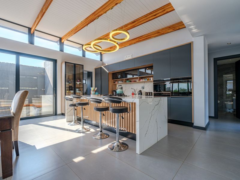 Modern open-plan kitchen featuring a marble waterfall island, timber ceiling beams, and large sliding doors leading to an outdoor area.