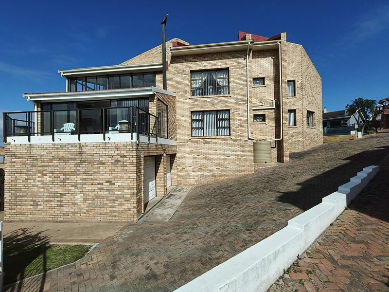 A multi-level face brick house featuring a paved driveway, double garage, and an elevated balcony with glass balustrades.