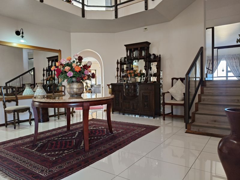 Spacious grand entrance hall featuring polished tiled flooring, a sweeping staircase with glass balustrades, and an open mezzanine level above.