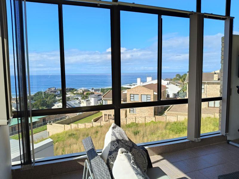 Enclosed balcony featuring large glass windows with expansive ocean and coastal views, tiled flooring, and vertical blinds.