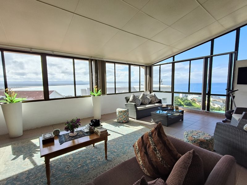 A bright, enclosed sunroom or patio featuring extensive glass windows with panoramic coastal views and tiled flooring.