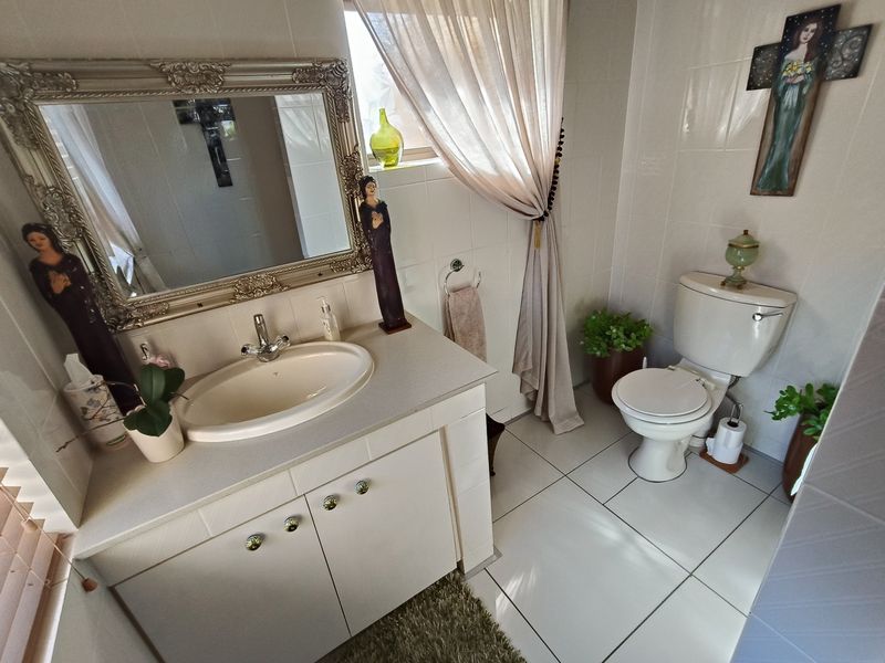A functional bathroom featuring a vanity cabinet with a basin, a wall-mounted mirror, and a standard toilet, finished with neutral wall and floor tiles.