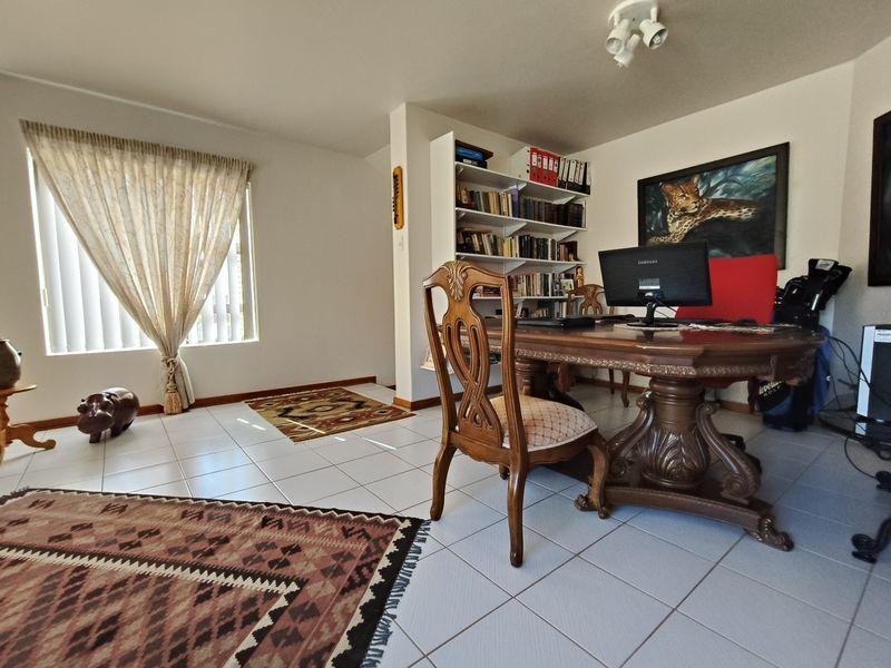 A functional home office space featuring tiled flooring, built-in shelving units, and ample natural light from the window.
