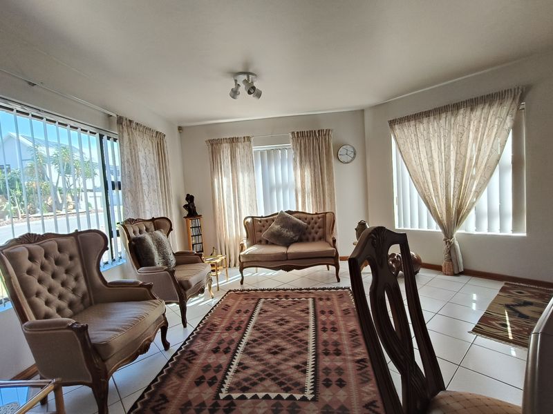 A bright living room featuring tiled flooring and large windows with security bars, offering a functional space with natural light.