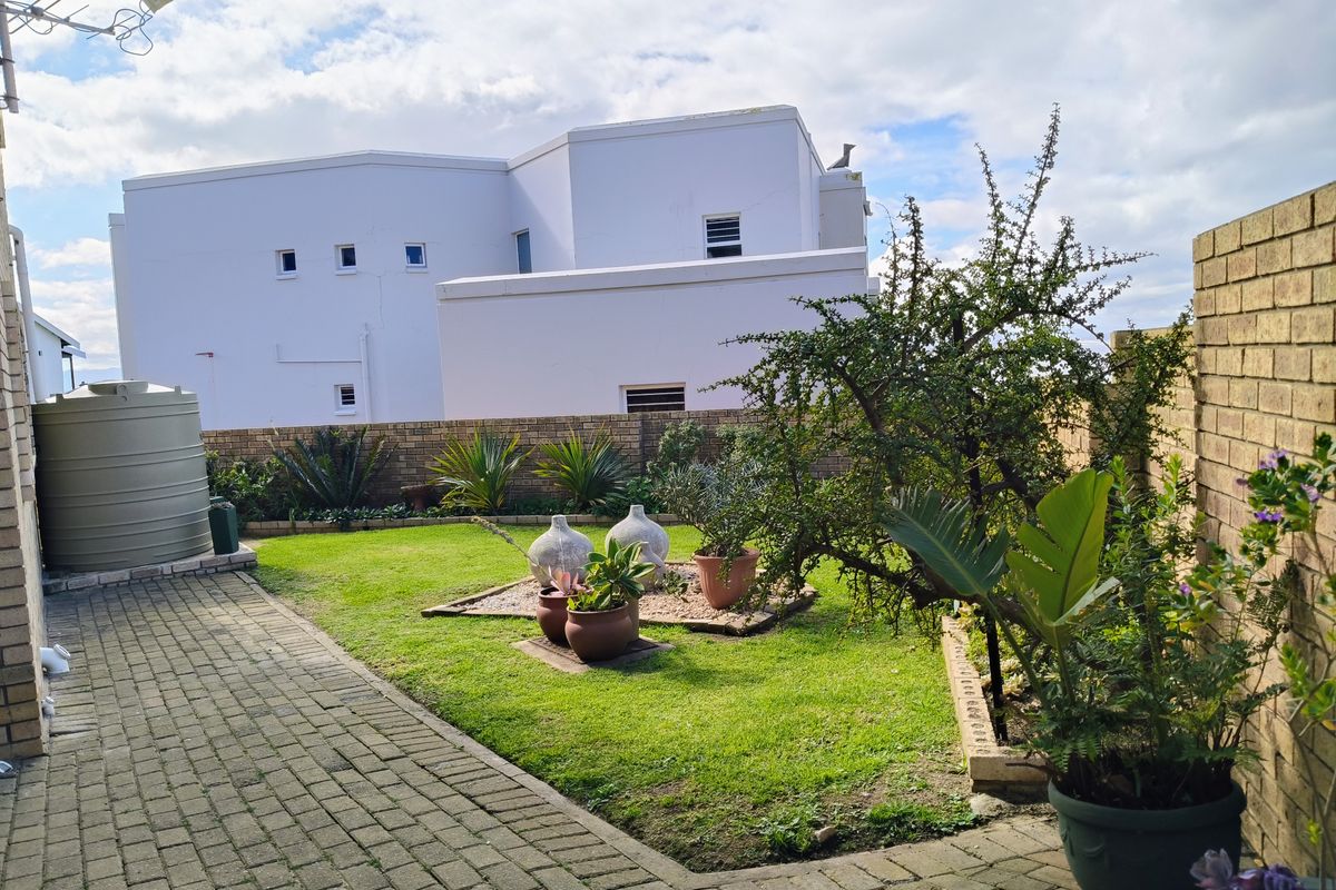 A private rear garden featuring a paved patio area, established lawn, and a brick boundary wall with an integrated water storage tank.