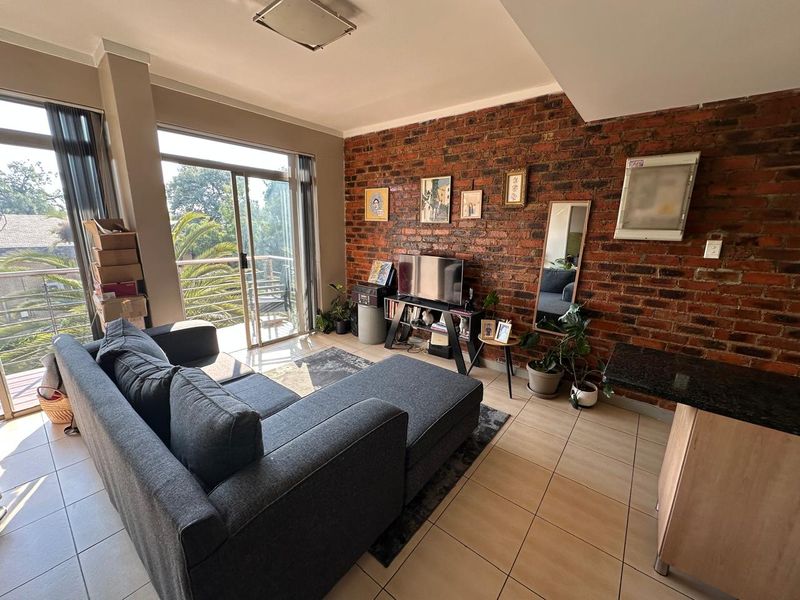 Open-plan living area featuring an exposed brick wall, tiled flooring, and large sliding glass doors leading to a balcony.