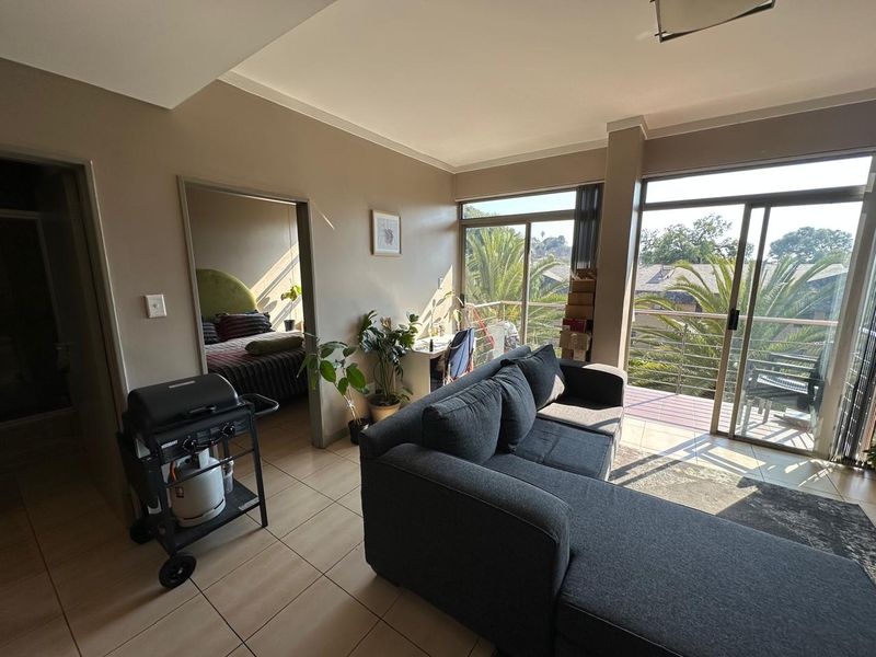 A living room featuring tiled flooring and large sliding glass doors that provide access to a balcony and natural light.