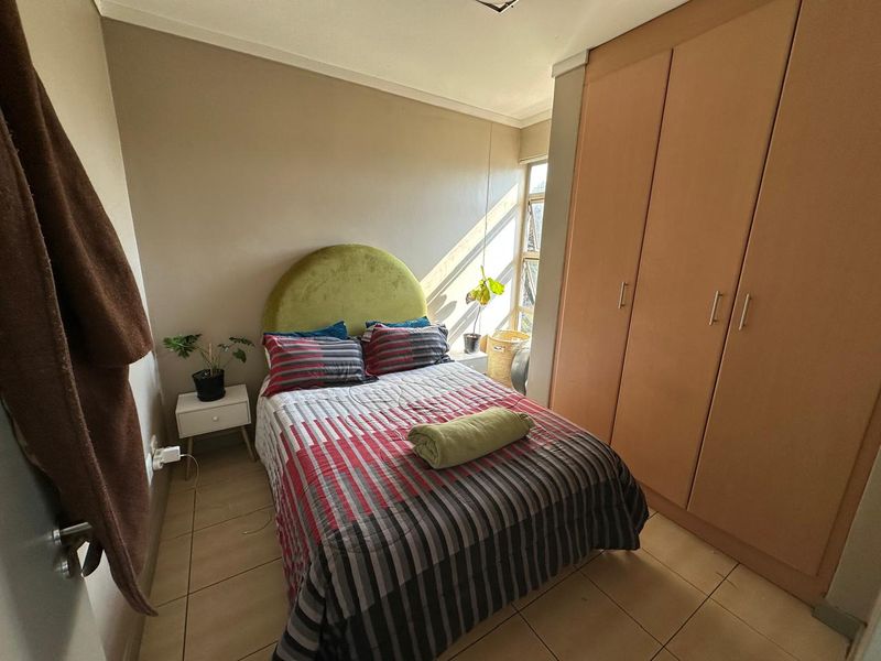 A compact bedroom featuring tiled flooring and built-in wooden cupboards, providing functional storage space.