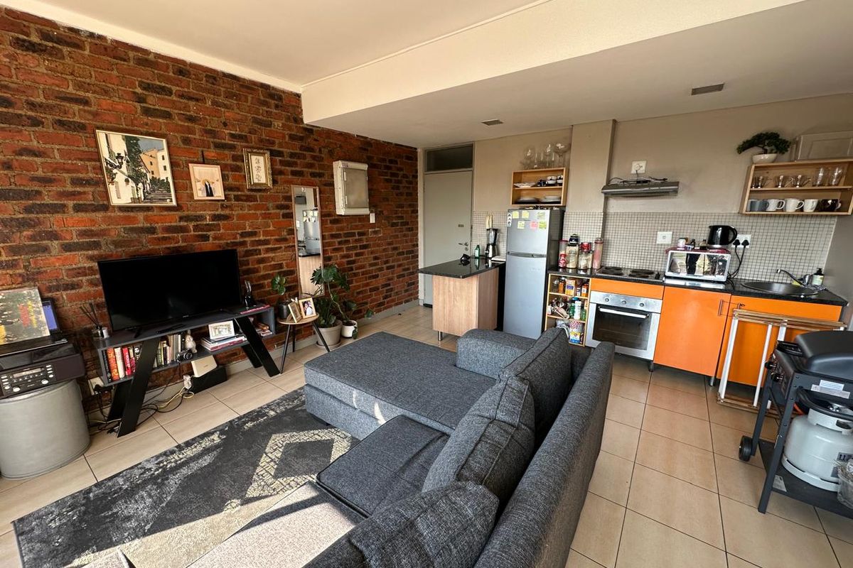 Open-plan living area featuring an exposed brick feature wall, tiled flooring, and a functional kitchen with built-in oven and extractor fan.