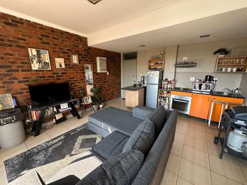 Open-plan living area featuring an exposed brick feature wall, tiled flooring, and a functional kitchen with built-in oven and extractor fan.