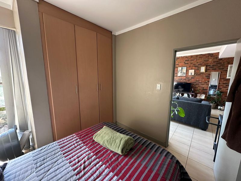 A bedroom featuring built-in wooden cupboards and tiled flooring, with a direct view into the adjacent living area.