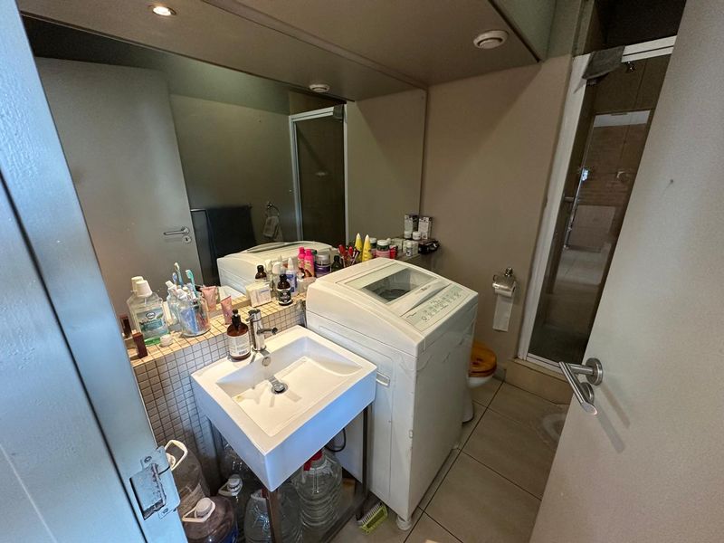 Compact bathroom featuring a wall-mounted basin with tiled splashback, large mirror, shower enclosure, and tiled flooring.