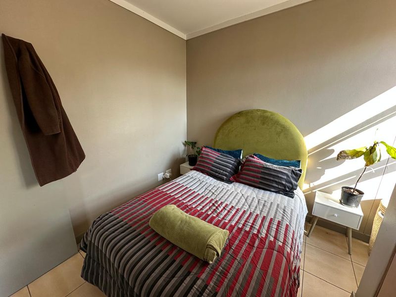 A compact bedroom featuring neutral wall tones and tiled flooring, offering a functional space with natural light.