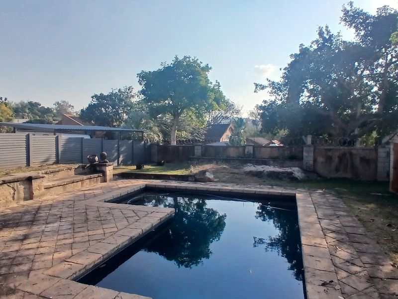 Outdoor pool area featuring stone paving, a perimeter wall with security fencing, and a built-in stone bench, set within a private garden space.