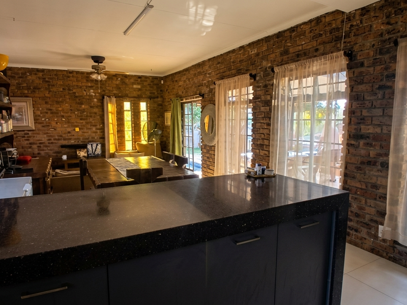 Spacious open-plan living area featuring exposed brick walls, a modern kitchen island with stone countertops, and large windows providing natural light.