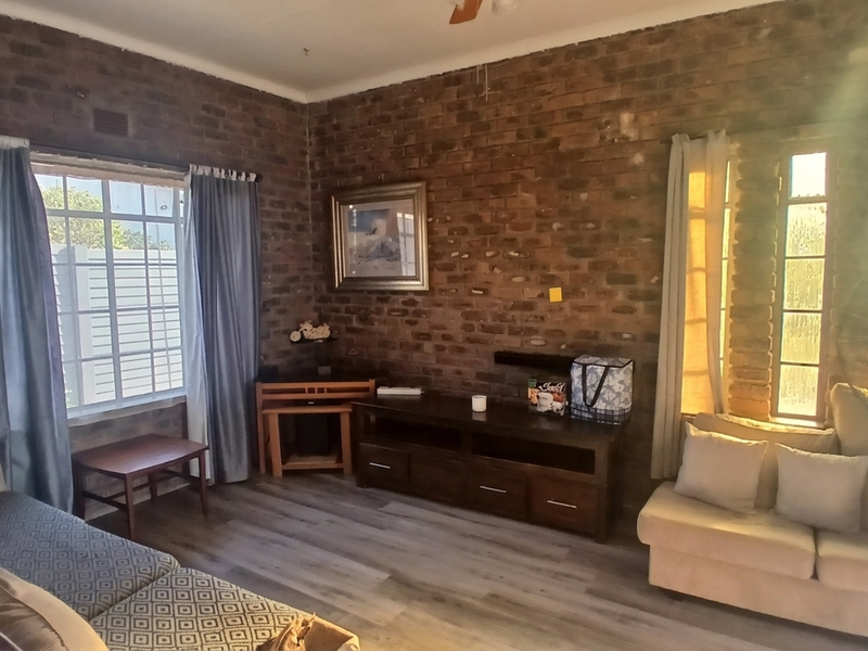 A living room featuring exposed brick walls, laminate flooring, and a ceiling fan, offering a rustic aesthetic with natural light.