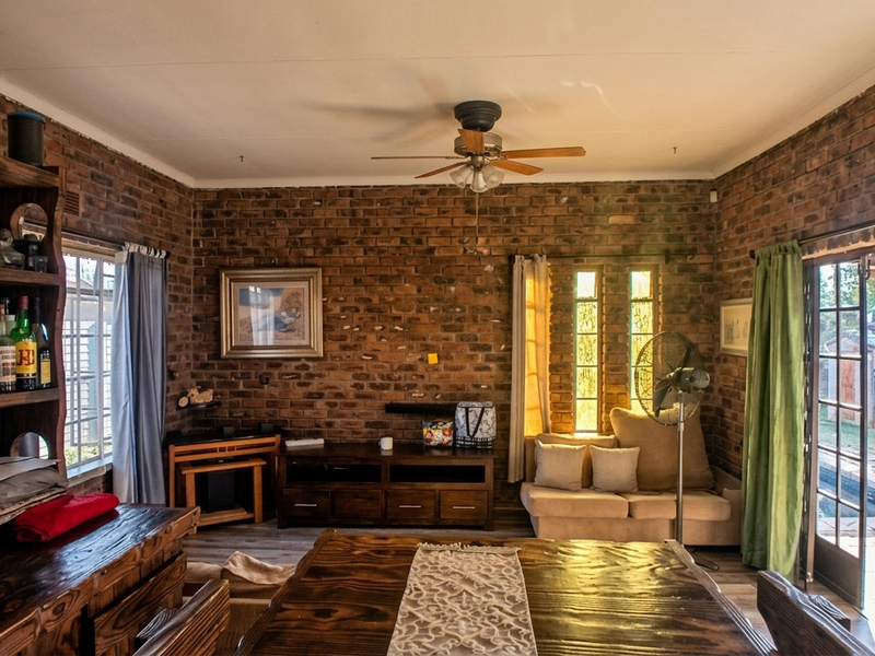 A rustic living room featuring exposed brick walls, a ceiling fan, and direct access to the outdoor area through glass-paned french doors.