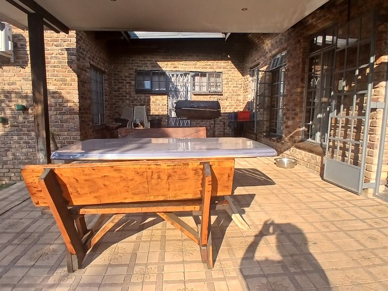 A covered outdoor patio area featuring exposed brick walls, paved flooring, and steel-framed windows, providing a functional space for outdoor living.