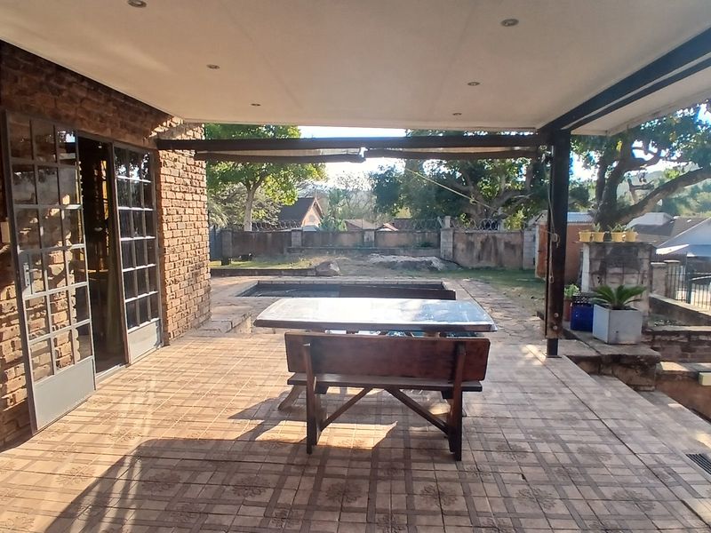 Covered outdoor patio featuring exposed brickwork, tiled flooring, and direct access to the garden and pool area through sliding glass doors.