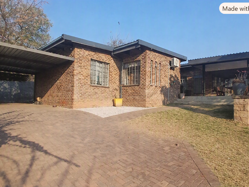A well-maintained brick house featuring a paved driveway, attached carport, and a covered patio area, set within a neat residential garden.
