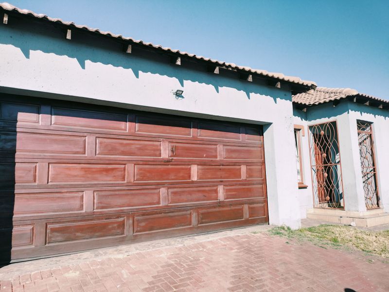 Exterior view of a residential property featuring a double garage with a wooden door, tiled roof, and a secure entrance gate.