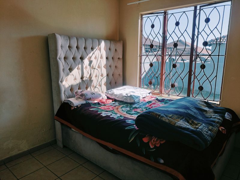 A bedroom featuring tiled flooring and security burglar bars on the window, requiring cosmetic updates to the wall finishes.